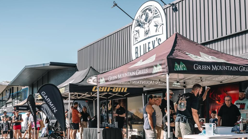 Outdoor event with people under tents branded with Garmin and Green Mountain Grills.